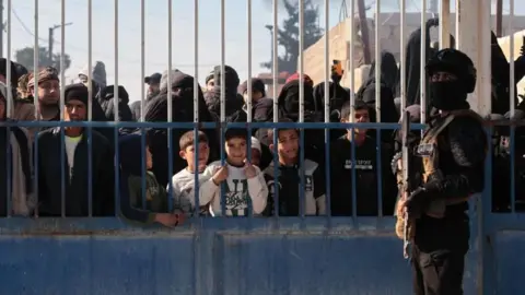 EPA man stands in front of gate with prisoners behind