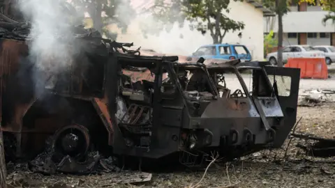 Reuters A destroyed anti-aircraft unit at La Carlota military air base. The metal has been blackened and twisted, and there is smoke rising from it. 