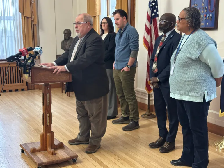 Mark Dion speaks at a podium, surrounded by city officials
