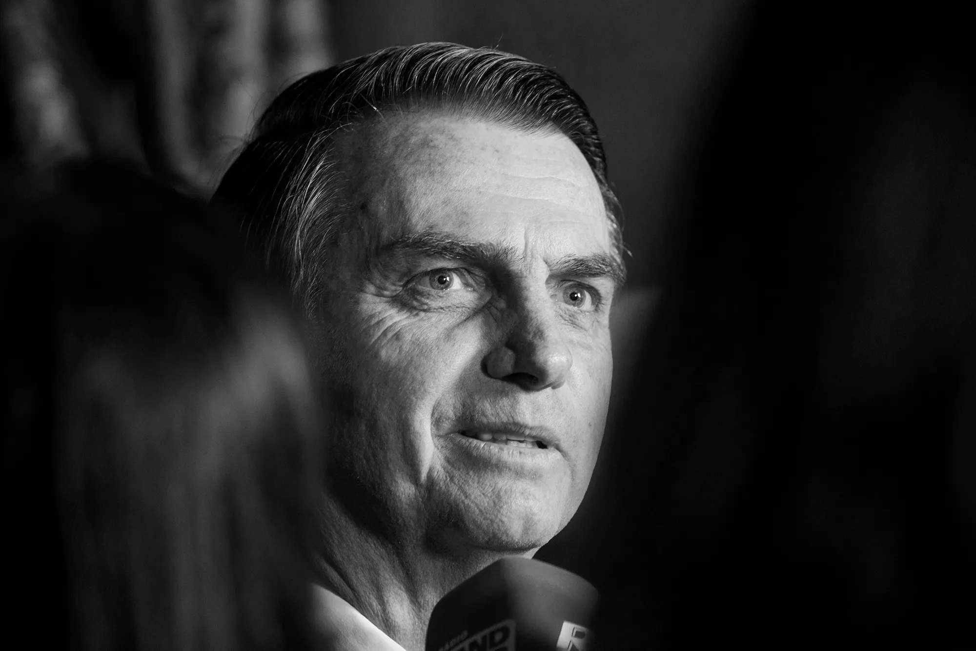 black and white photo of Jair Bolsonaro speaking into a microphone