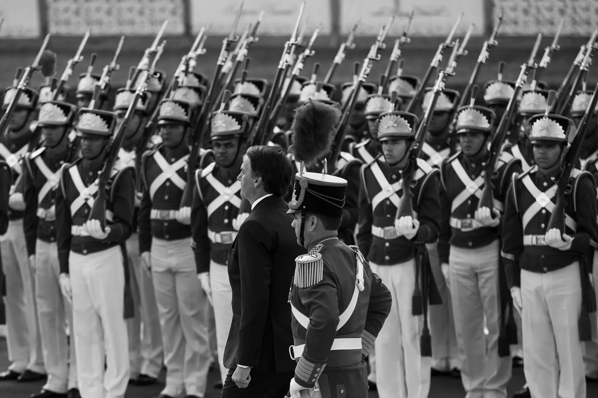 Soldiers in dress uniforms stand at attention as Bolsonaro passes.
