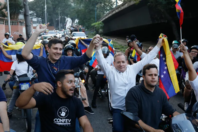 Juan Pablo Guanipa and Jesus Armas ride on the backs of motorcycles in a parade