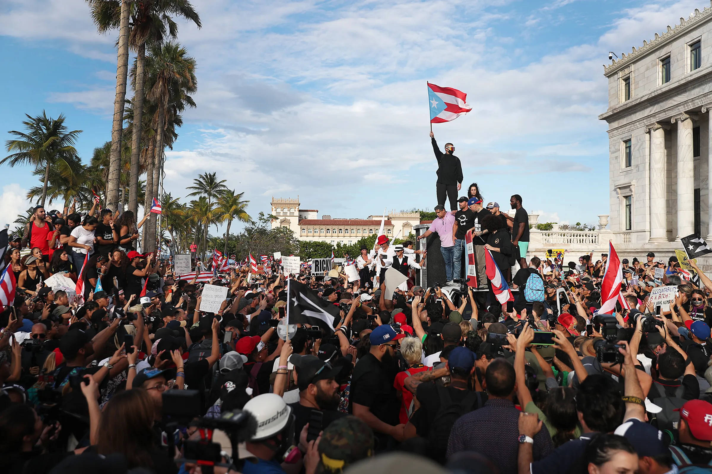 Bad Bunny raises the Puerto Rican flag as Ricky Martin and Puerto Rican rapper Residente address a crowd from atop a vehicle.