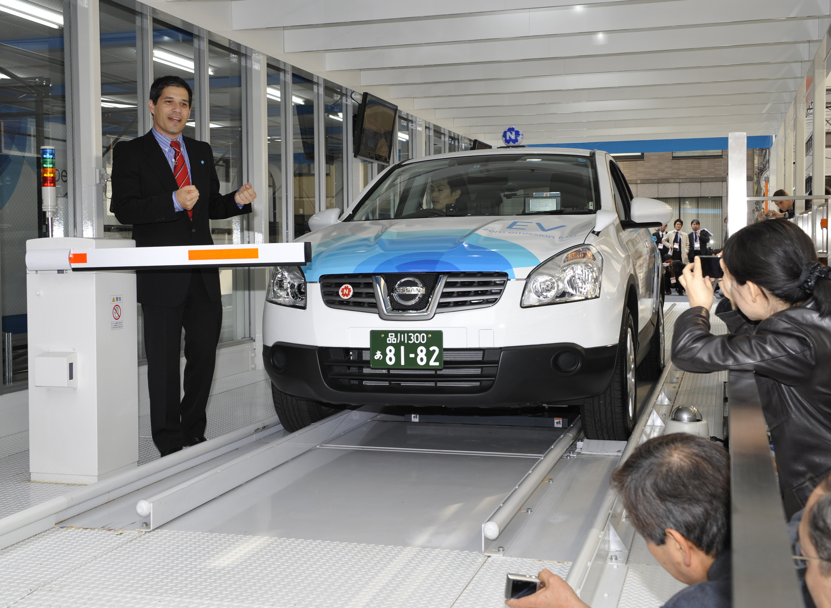 A man stands next to a compact electric car, inside a white-painted facility