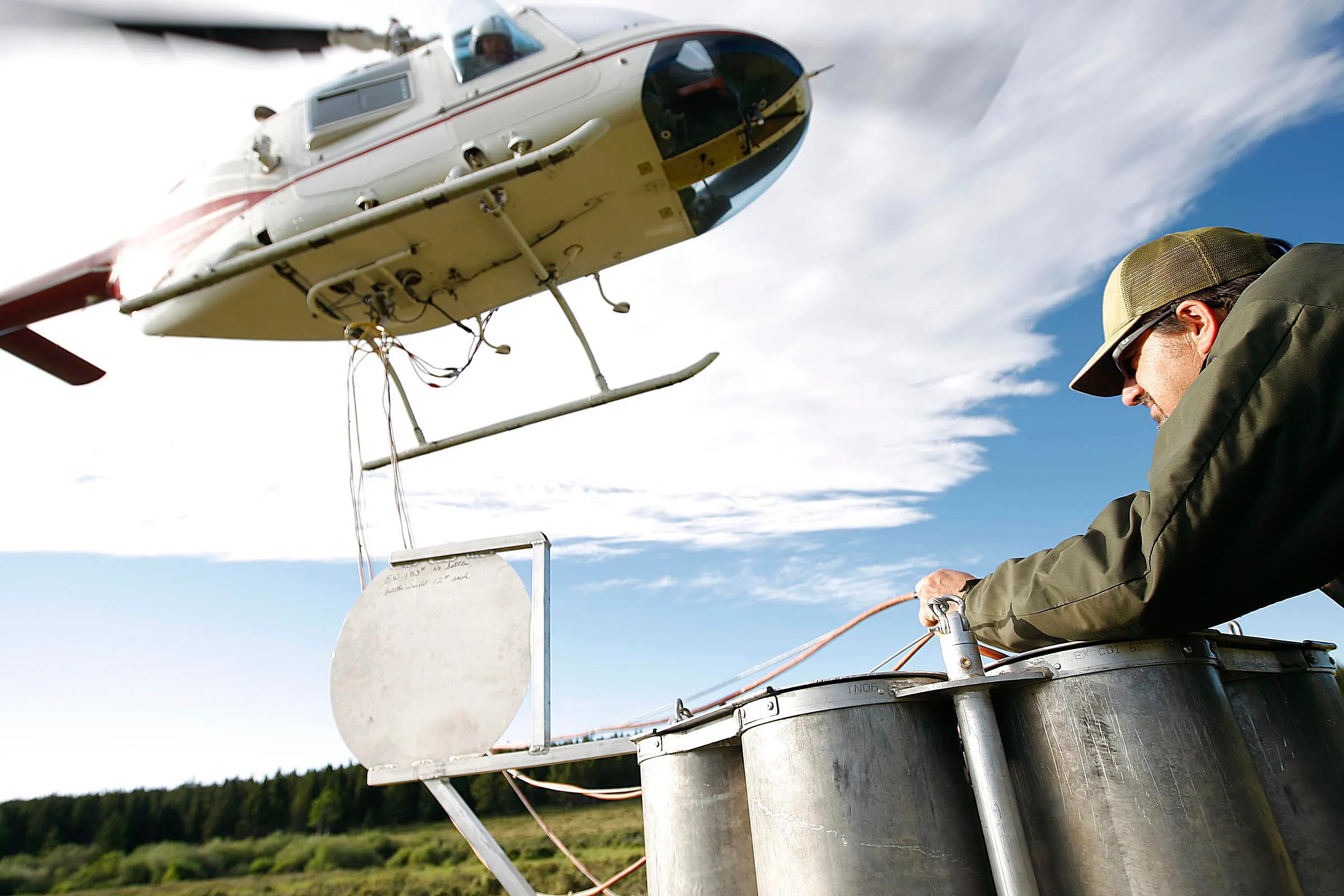 A man holding cords attached to a helicopter to stock mountain lakes