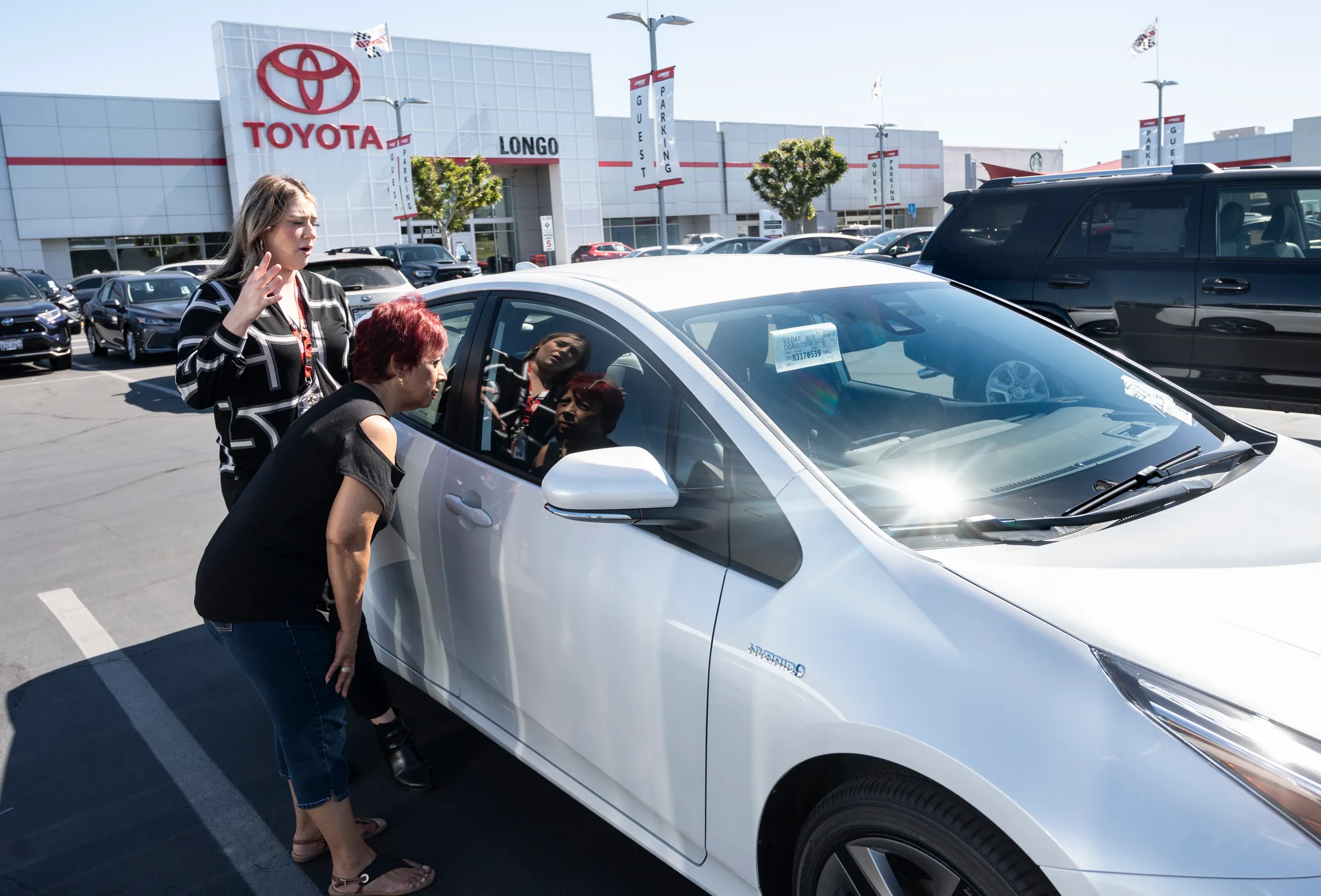 a customer is shown a 2022 white toyota prius car at a toyota dealership lot outdoors