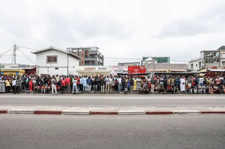 Supporters of incumbent President of the Republic of Congo and presidential candidate Denis Sassou Nguesso stand on the side of the road as they wait fot him to arrive at a polling station in Brazzaville on March 15, 2026 during the Republic of Congo's presidential elections. (Photo by Daniel BELOUMOU OLOMO / AFP)