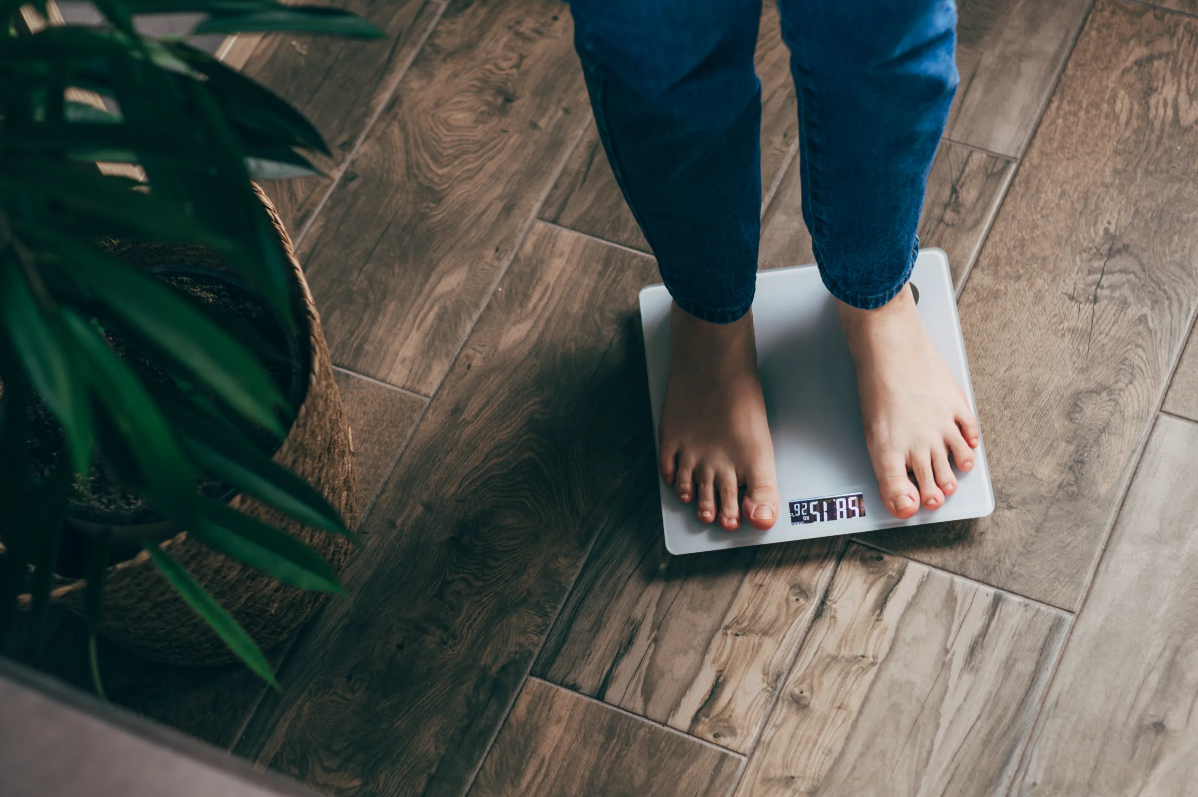 A person with bare feet stands on a scale on a hardwood floor.