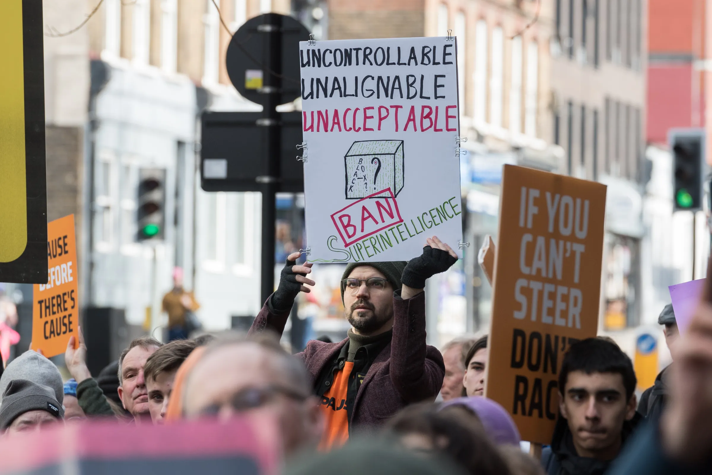 A man holds up an anti-AI sign at a protest outside of OpenAI’s headquarters. The sign says uncontrollable, unalignable, unacceptable. Ban superintelligence.