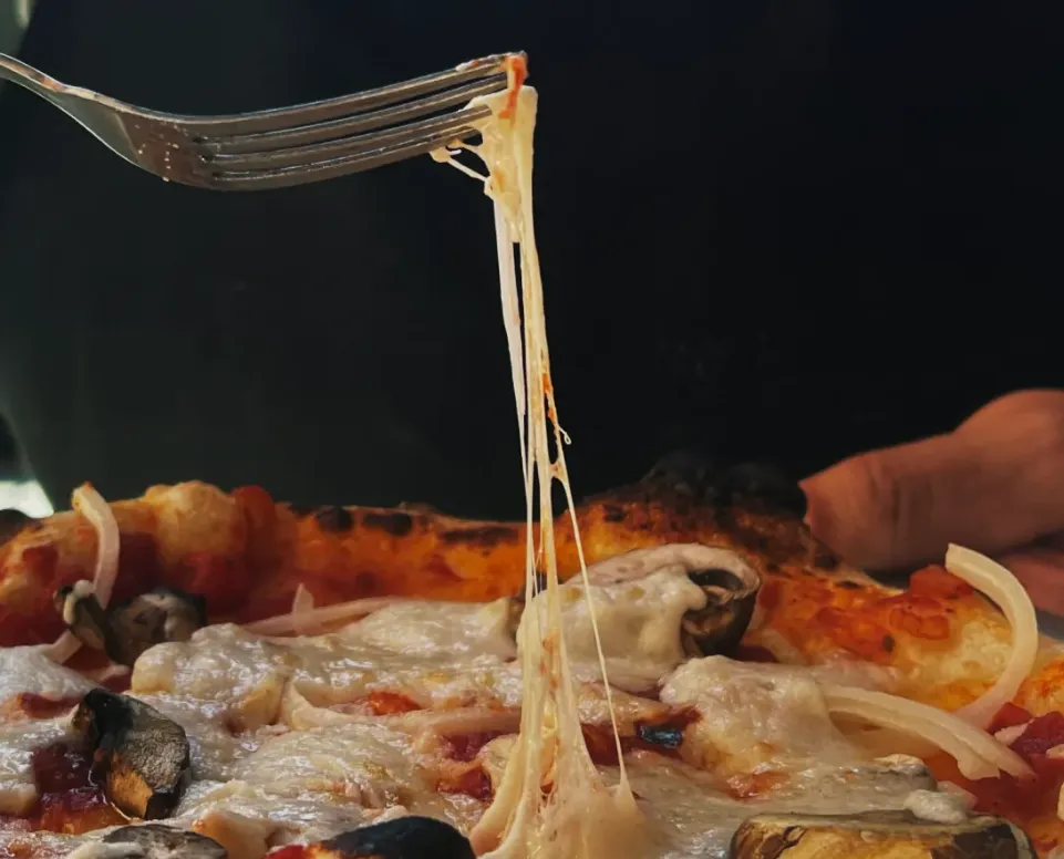 A close-up of a fork pulling stretchy dairy-free mozzarella cheese up off of a pizza.
