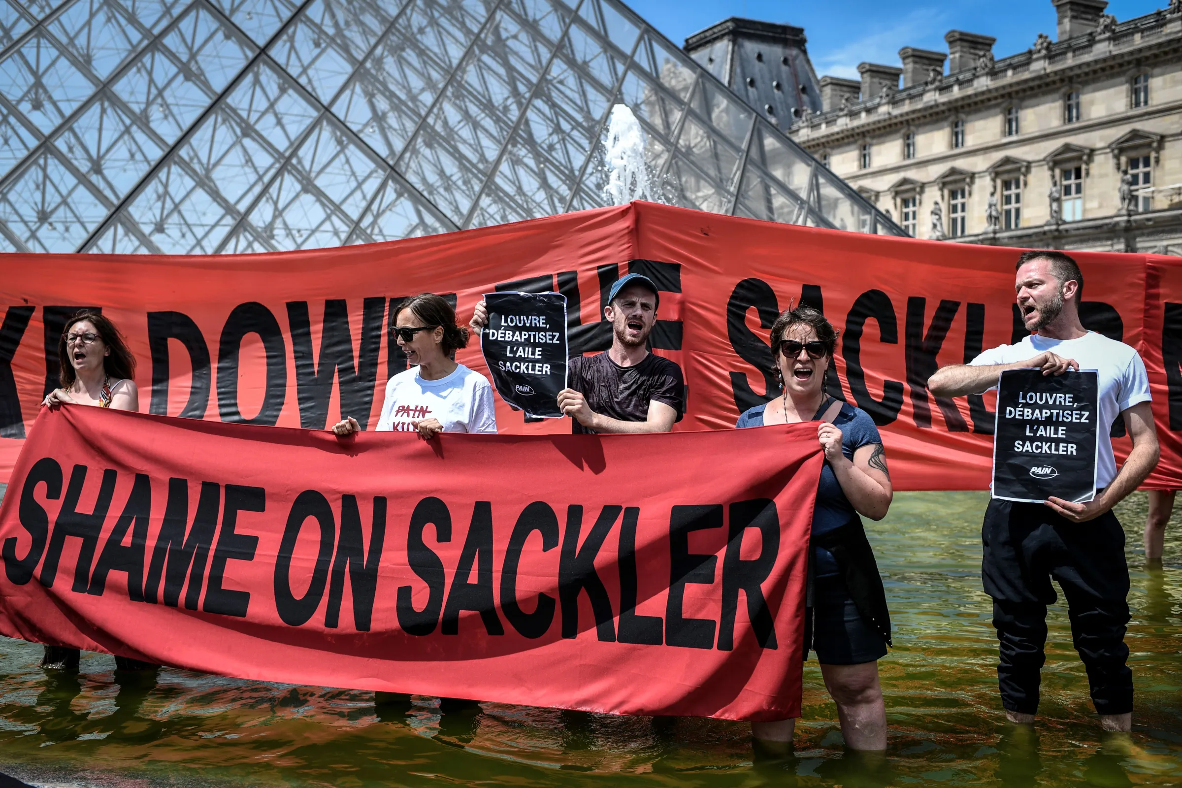 Protesters stand outside of the Louvre holding a red sign saying ‘Shame on Sacklers’