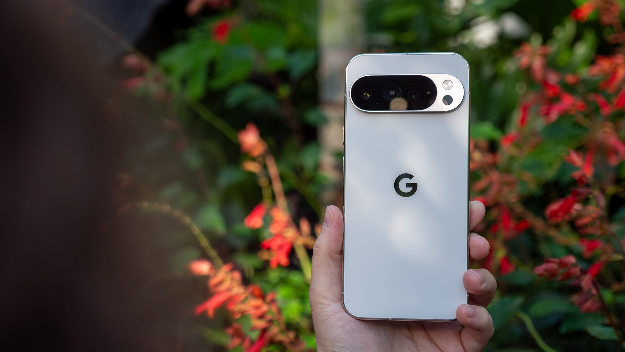 Holding a white Google Pixel 10 Pro XL in front of red flowers