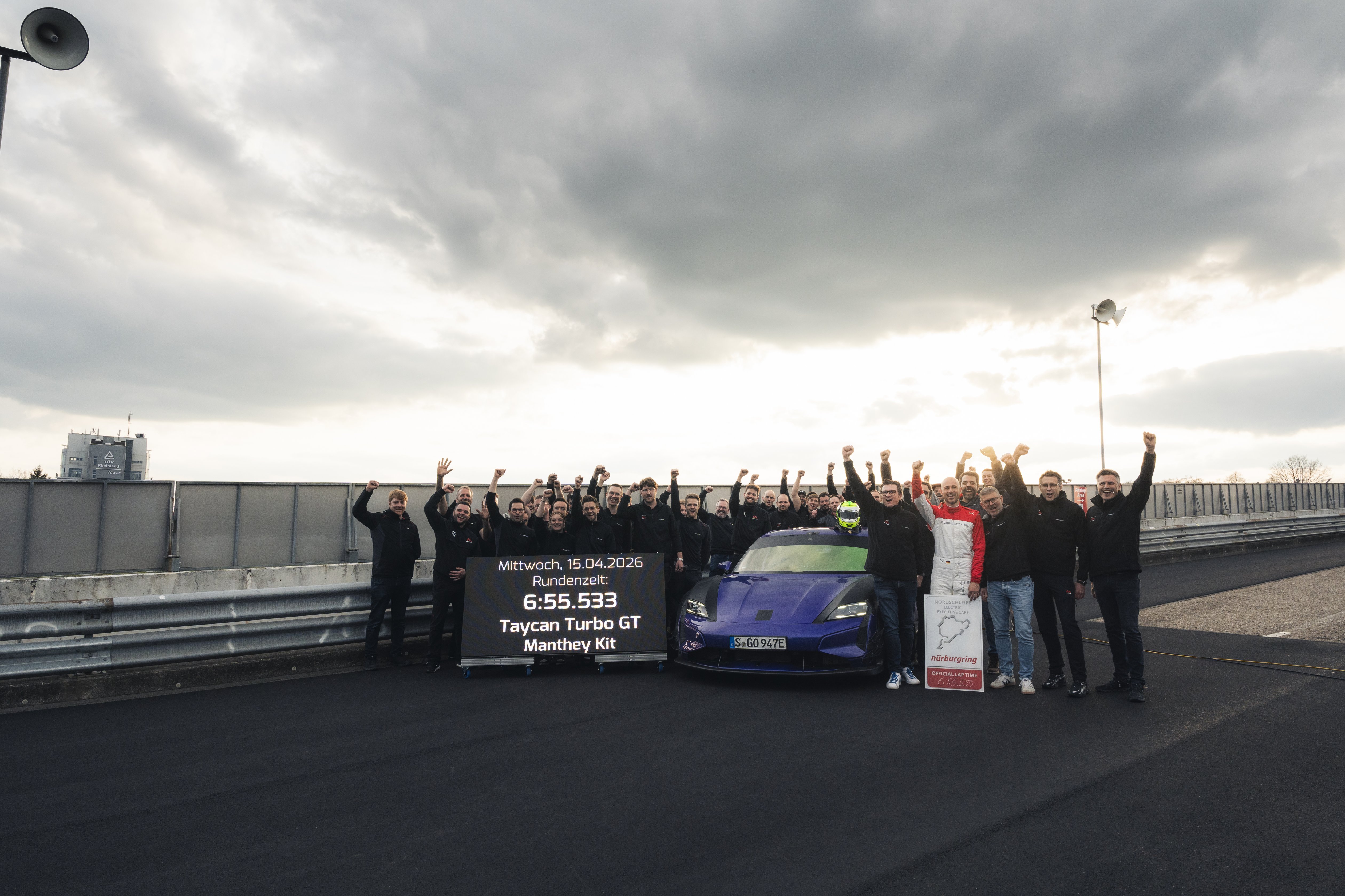 A team of people pose by a car in the pitlane