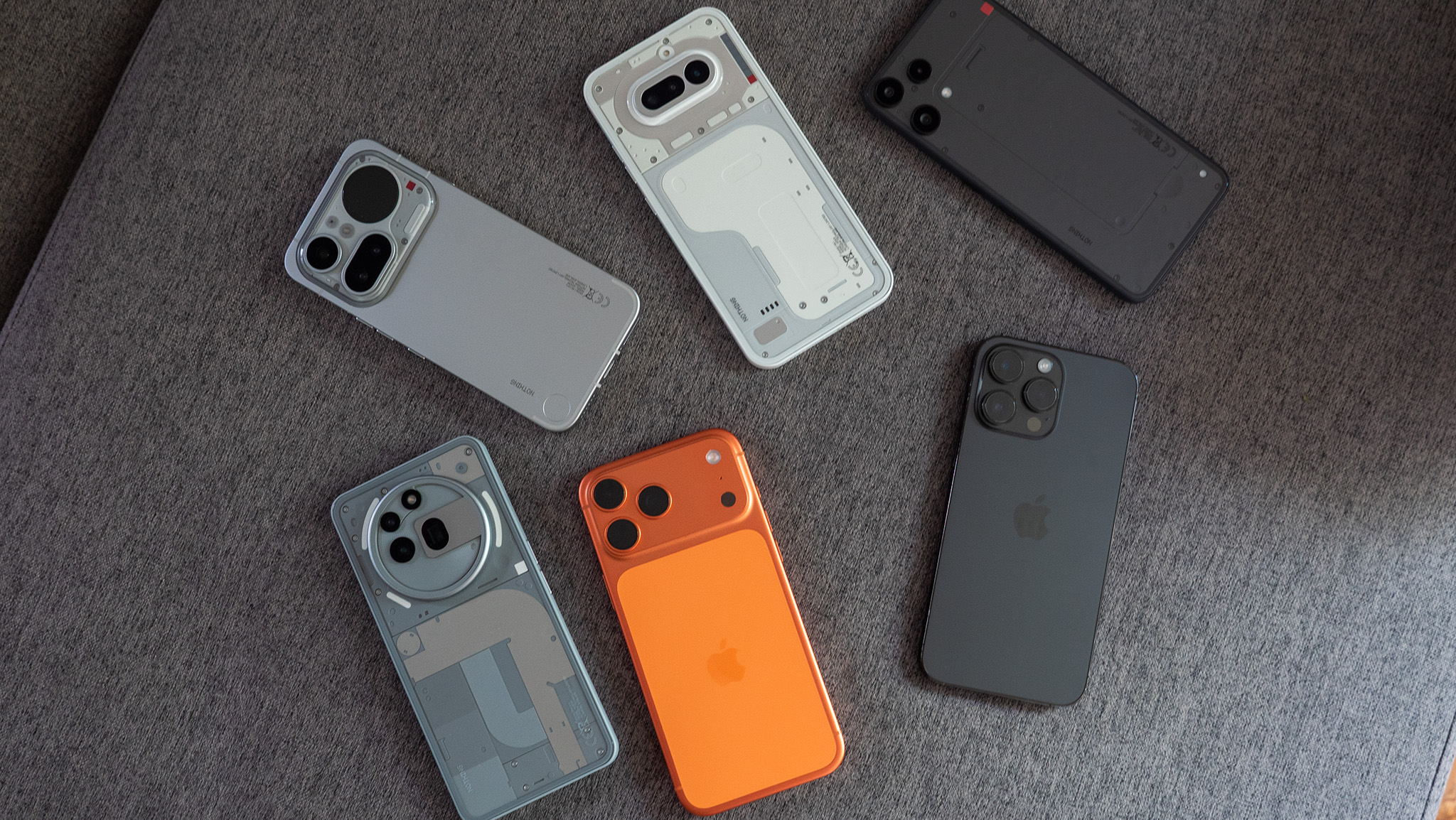 A Nothing Phone 3a Lite, 4a, 4a Pro, 3a Pro, and iPhones 14 and 17 on a grey couch
