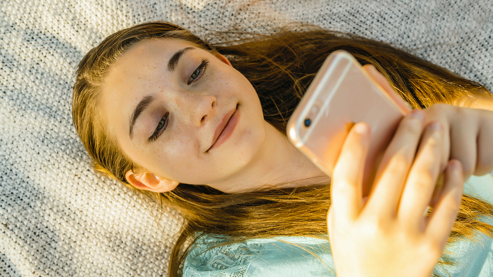 Smiling teenage girl looking at her smartphone in bed