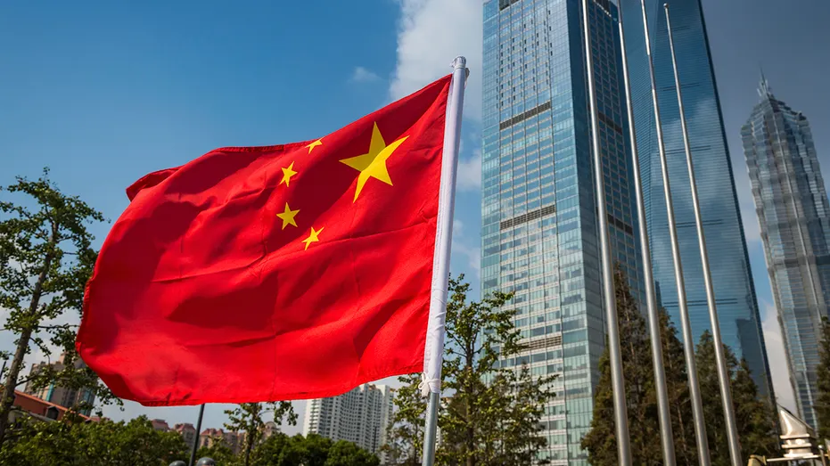 The vibrant red field and yellow stars of the Flag of the People's Republic of China flying in the breeze beside the futuristic glass and steel towers of Pudong's soaring skyscrapers, Shanghai, China.
