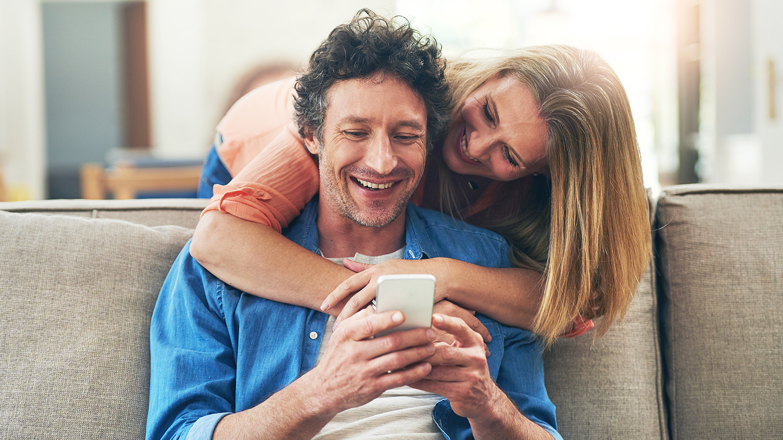 Couple on sofa looking at a smartphone, smiling