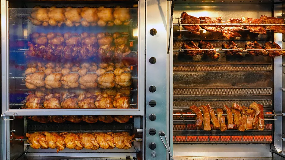 Rotisserie chickens roasting on spits inside a commercial oven at a grocery store deli.