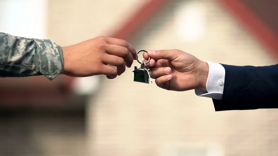 A service member receives house keys from a real estate professional. VA-backed mortgages are becoming more common as high housing costs push eligible military buyers to seek lower upfront costs.