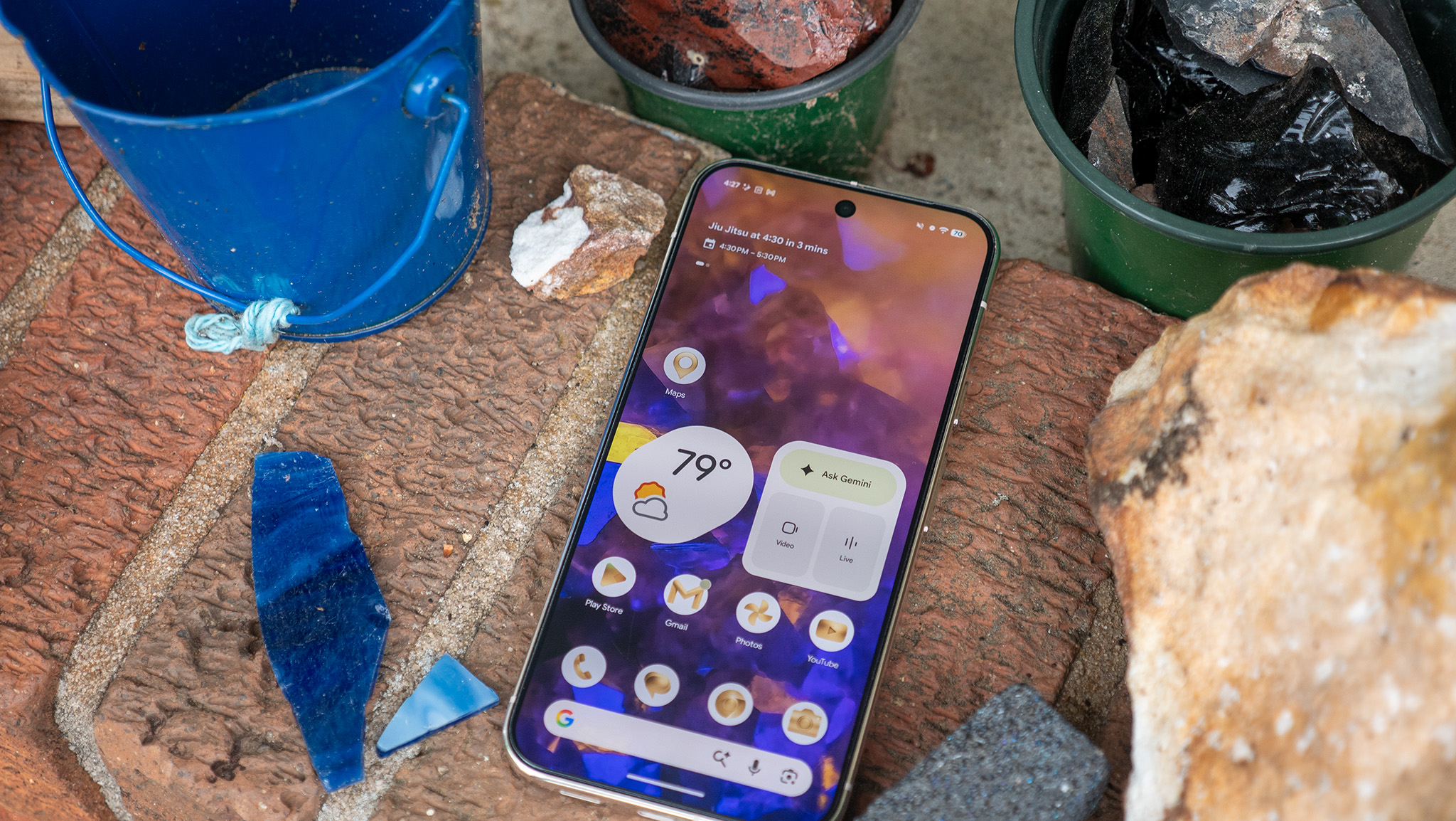A Google Pixel 10 Pro XL using a Gemini-generated gem theme pack and wallpaper, surrounded by rocks and gems