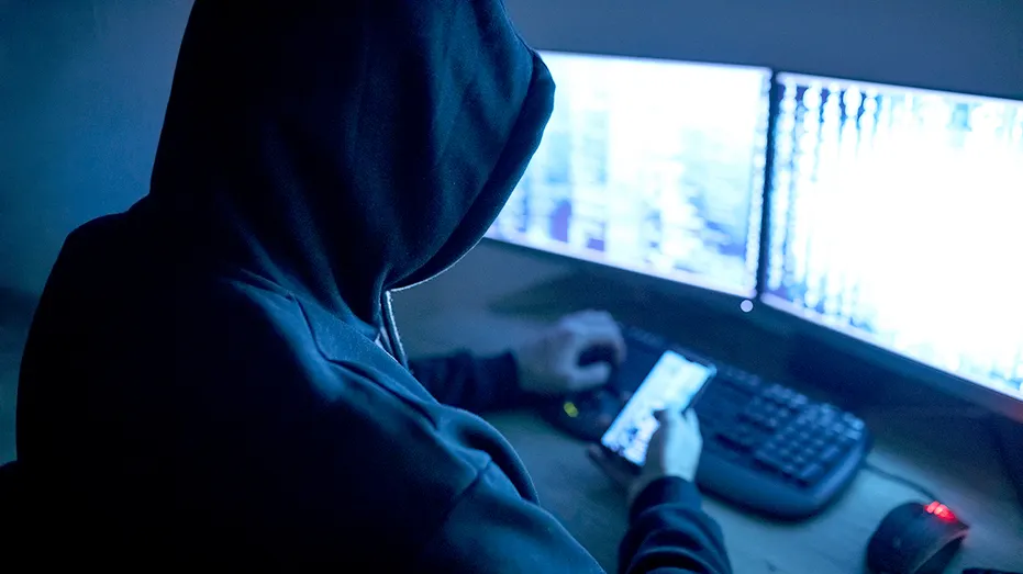A hacker using a phone and computer.