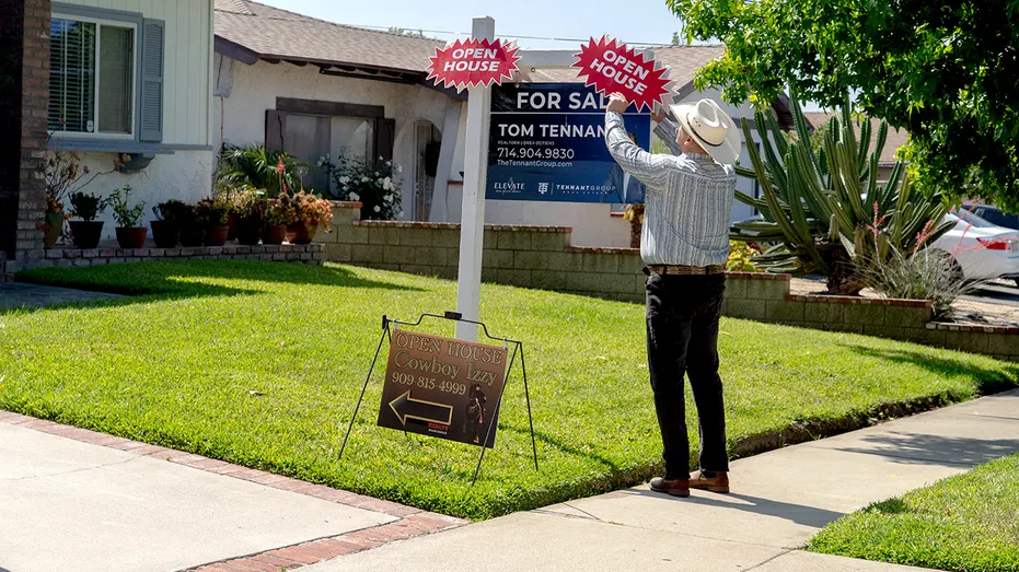 A real estate agent adjusts a sign outside a home.