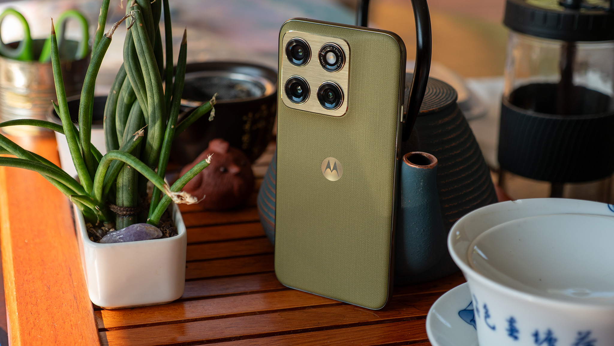 The back of the olive green Motorola Edge 2026 on a tea table next to a potted plant