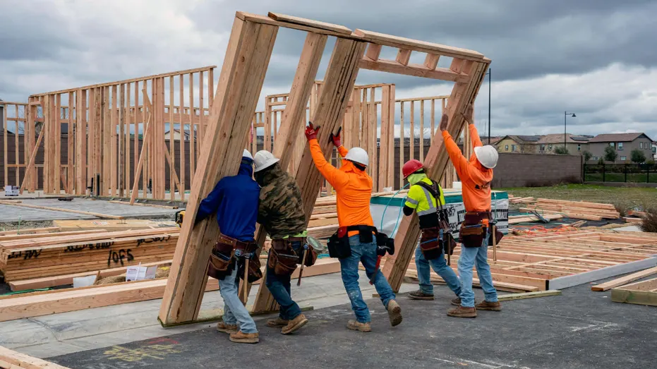 Builders lift wood frames that are part of a home.