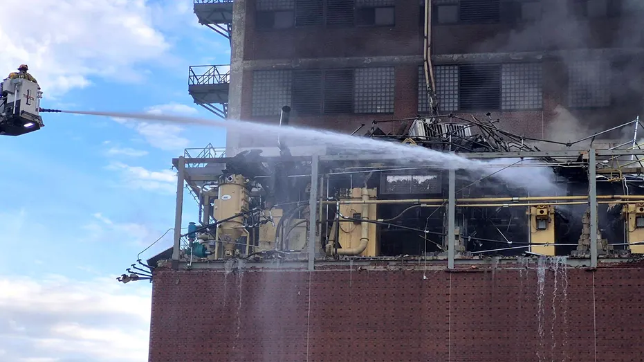 Firefighters use a water hose near a plant after an explosion and fire