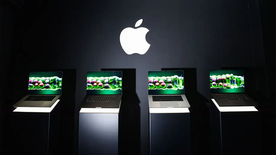 Four Apple MacBook Pro laptops displayed on illuminated stands beneath a large Apple logo