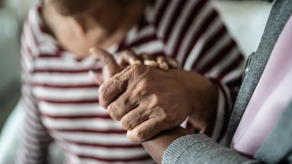 Nurse or home caregiver and senior woman holding hands at home