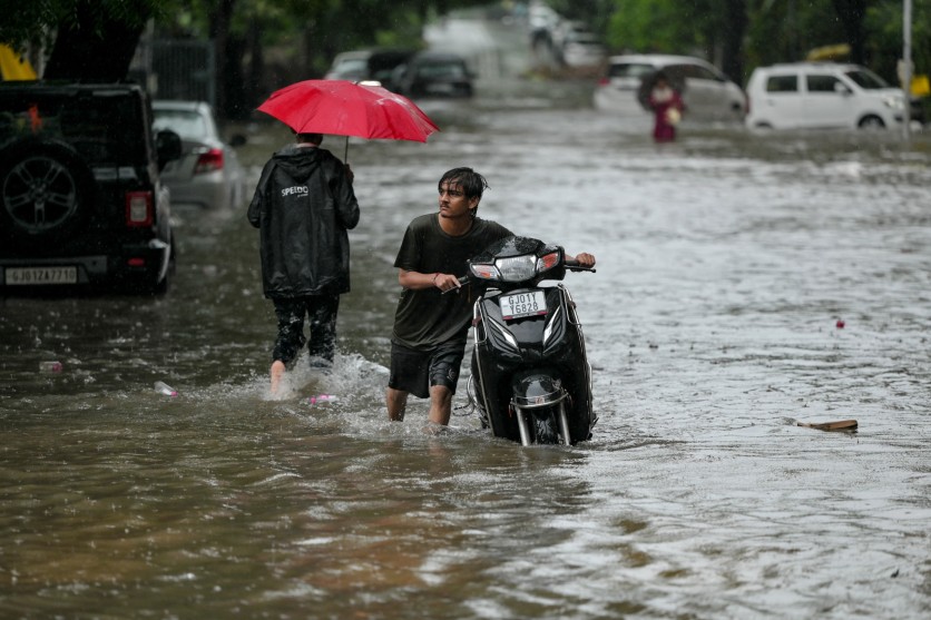 A man pushes his scooter through a water-logged street during rainfall