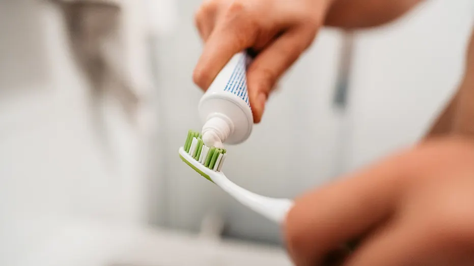 Young Man Putting On Toothpaste To Brush His Teeth In The Bathroom