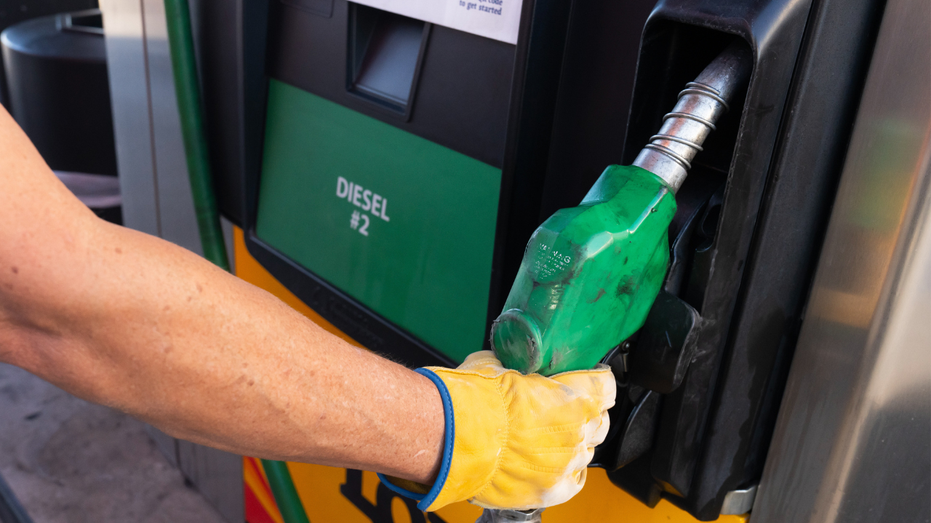 A person is seen grabbing the nozzle for diesel fuel at a gas station.